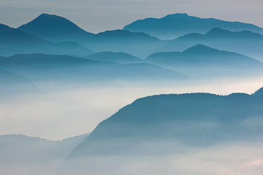 Mountain ridges emerge through atmospheric morning mist, offering serene nature tourism exploration in the Julian Alps Natural Park, Alba Valley, Friuli Venezia Giulia, Italy. (174 characters)