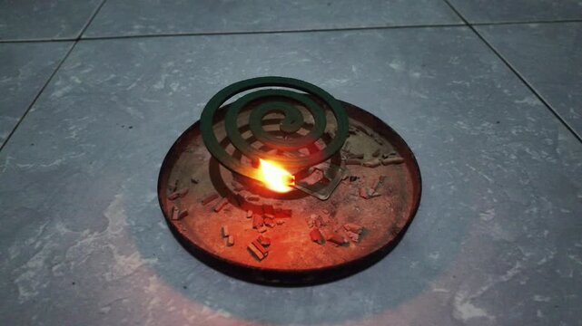 Burning green mosquito coil spiral with glowing orange ember on a metal tray for insect repellent protection at night