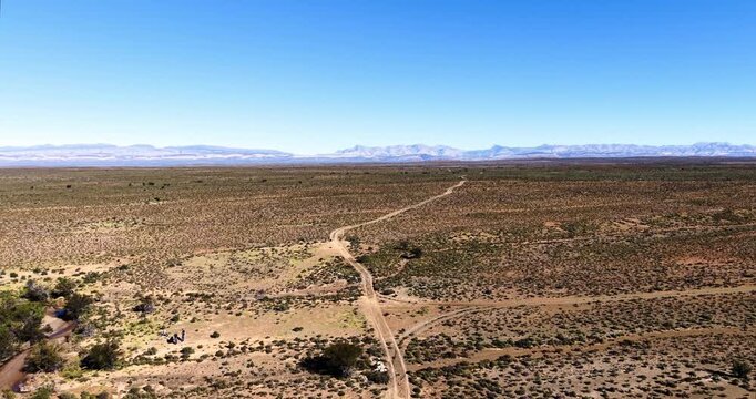 Expansive aerial panorama of the Great Karoo featuring a remote gravel road, seasonal watercourse and the distant Swartberg Mountain range, an iconic semi-arid landscape.