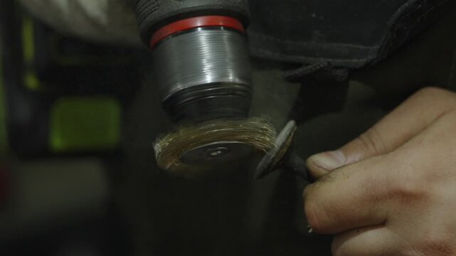 Close-up of mechanic cleaning metal part with rotating wire brush.