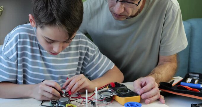 Father and son engage in electronics project. Dad and kid explore circuits using multimeter and components. Learning fosters strong bond. Educational activity promotes creativity and collaboration