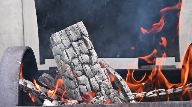 Single wooden log burning with bright orange flames in an outdoor grill, campfire and cozy summer night concept