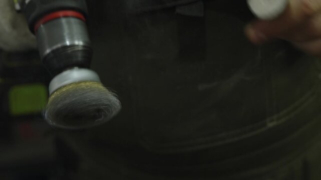 Close-up of mechanic cleaning metal part with rotating wire brush.