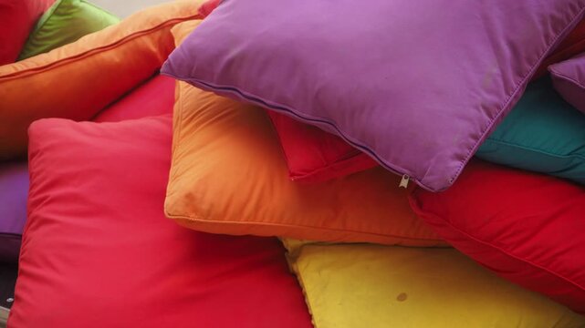 Close up vibrant colored pillows stacked up high creating soft cushioned surface perfect for relaxation or playful setting slow motion camera movement