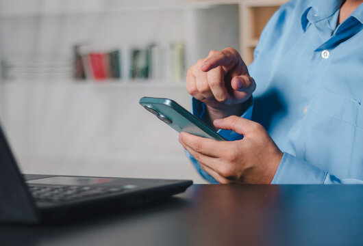 Businessman using smartphone while working on a laptop, representing mobile technology, digital communication, online productivity and remote workflow in a modern office environment. Life style