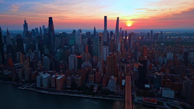 Flight over the Queensboro Bridge at sunset time. City skyline against pink sky.