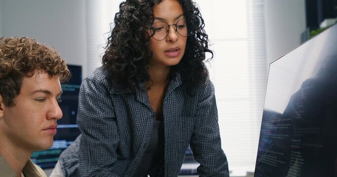  Hispanic man and woman programmers discuss application design and security while coding on monitors planning deployment and sharing advice on AI and database solutions