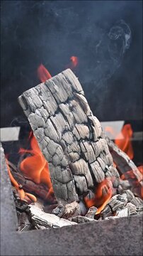 Single wooden log burning with bright orange flames in an outdoor grill, campfire and cozy summer night concept