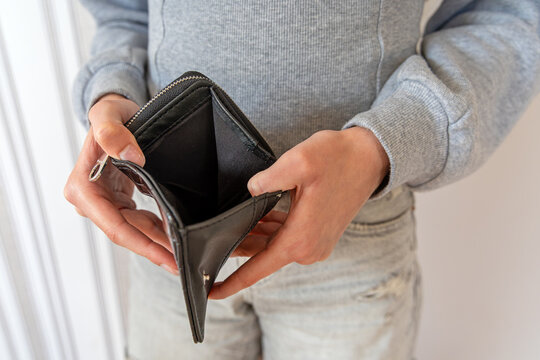 Person Holding Open Empty Black Wallet. Close-up of a person holding open an empty black zippered wallet with bare compartments while wearing a gray sweatshirt indoors.