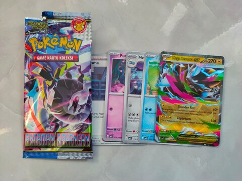 Malang, Indonesia - July 21, 2026: An opened Indonesian Pok&eacute;mon booster pack rests beside five overlapping trading cards, showcasing a colorful Mega Zeraora EX. Ancaman bayangan (Shadow threat).