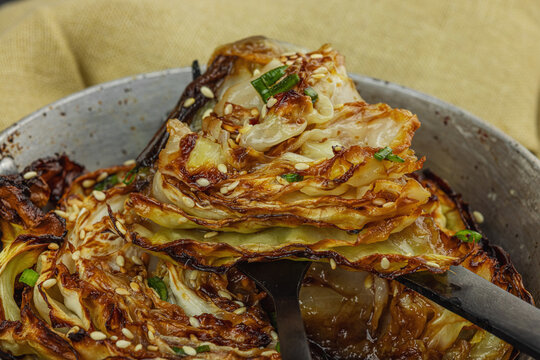 Roasted cabbage steak with Asian glaze, sesame seeds, and green onion in frying pan, dark background