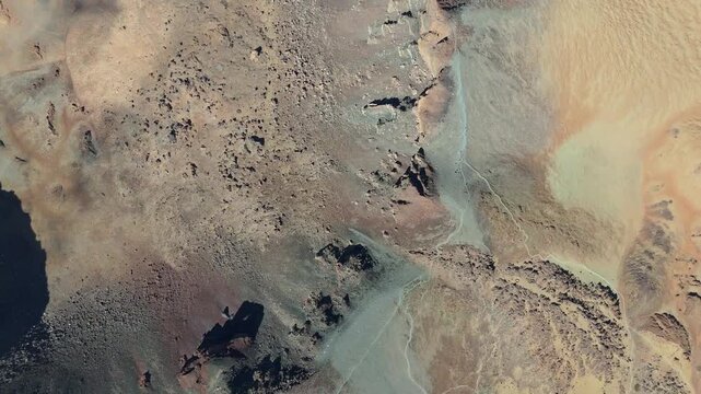 Aerial drone shot pulling back from a rugged, arid volcanic landscape around Pico Viejo on Tenerife, Canary Islands. The sun casts sharp shadows on the rocky, sandy terrain.