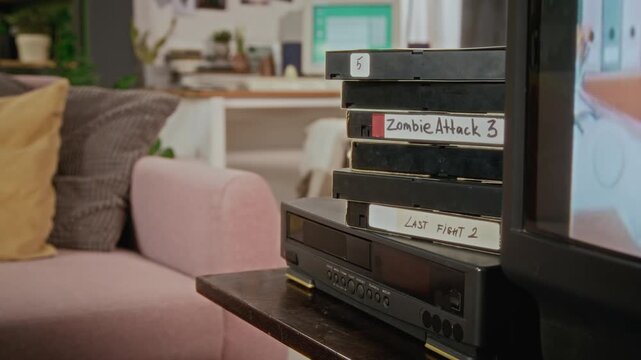 Retro VHS tapes sitting stacked on VCR player next to flickering CRT television in living room. Ideal for retro marketing, vintage media documentaries, or 90s themed commercial projects
