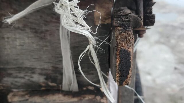 A close up of a frayed white rope hanging from a piece of weathered wood