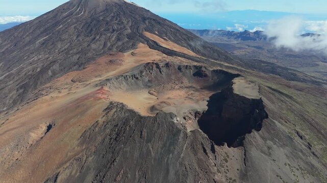 An aerial drone shot pans left and booms down over the rugged volcano Pico Viejo of Tenerife. The majestic mountain peak and its vast crater are illuminated by the bright sun.