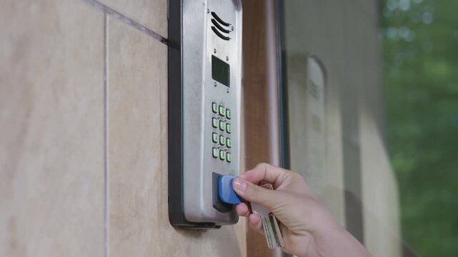 Security access control panel mounted on wall, showing keypad and display, as a hand approaches with a keycard for entry in a residential setting