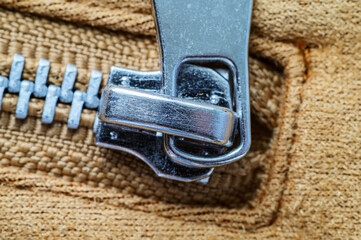 Close-up view of a shiny metal zipper pull and teeth on textured fabric © dimas830