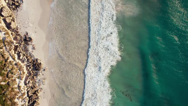 Waves roll onto the sandy shore of North Beach as clear turquoise water meets the rocky coastline at sunrise