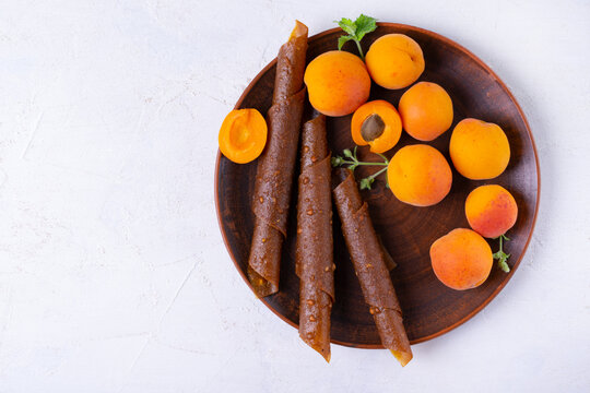 Fruit pastila or smokva with apricot and apple on a clay plate on a white table. Top view. Natural rolled dessert made of dried pureed fruits. Copy space