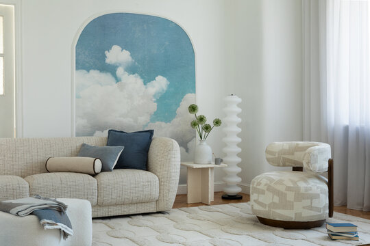 Modern living room interior with a cozy sofa, unique armchair, and cloud mural on a bright wall with natural light