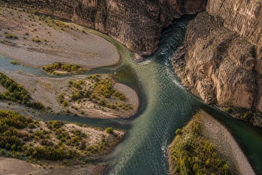 River tributary merging seamlessly with main stream at canyon entrance, aerial view.