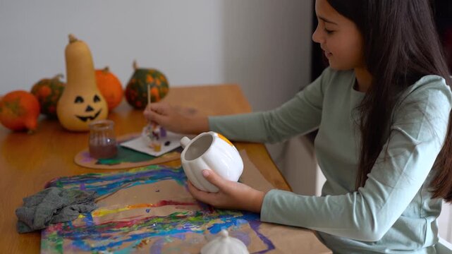 Female child painting on a pumpking cup during fall season for Halloween event - Holiday, childhood and autumn lifestyle concept