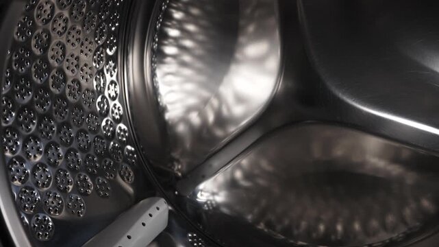 Empty stainless steel washing machine drum inside view close up.
