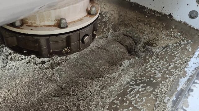 Mixing process of lightweight polystyrene concrete with a visible rotating screw auger inside the hopper.