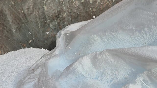 Slow motion shot of lightweight polystyrene beads pouring into a bucket and sucked by a vacuum hose.