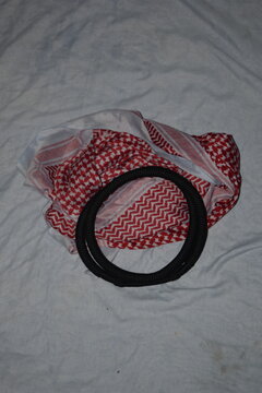 Classic Saudi Arabian white patterned shemagh black agal headband arranged on a white cloth for cultural attire display.

