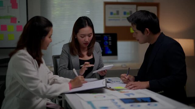 Asian business team brainstorming and planning a new project during a late-night meeting, collaborating and discussing strategy with financial charts and documents