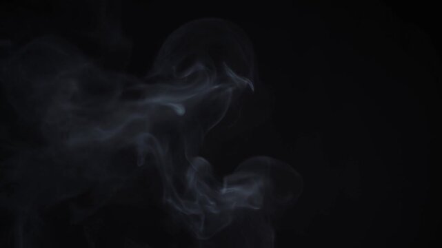 Slow motion tracking of smoke swirling and drifting against dark studio background