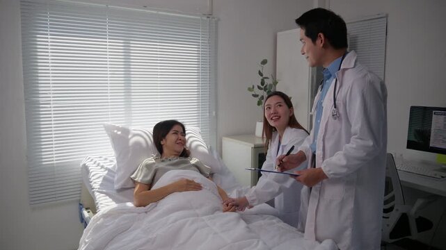 Two asian doctors talking to a female patient in a hospital room, reassuring and explaining the diagnosis and treatment while holding her hand and smiling