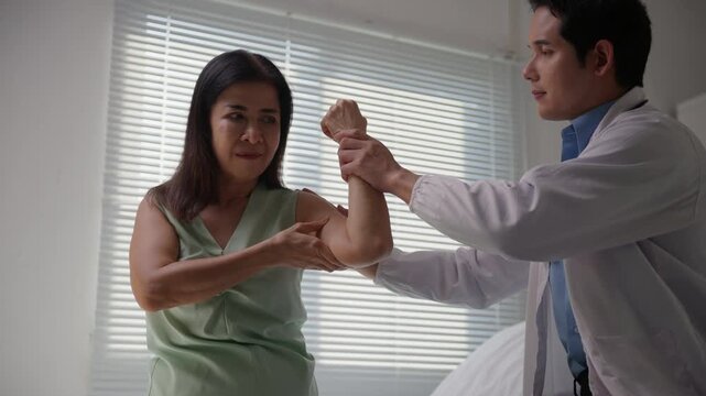 Young physiotherapist examining an elderly asian woman's arm and elbow in a clinic, providing physical therapy and rehabilitation care for her muscle injury and joint pain