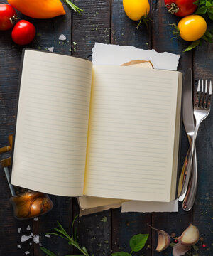 Open blank recipe book with cooking ingredients on dark wooden background, top view with copy space for menu design