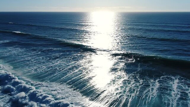 Aerial view of ocean waves crashing with bright sunlight reflecting on the water
