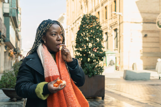 African woman eating an orange on city street
