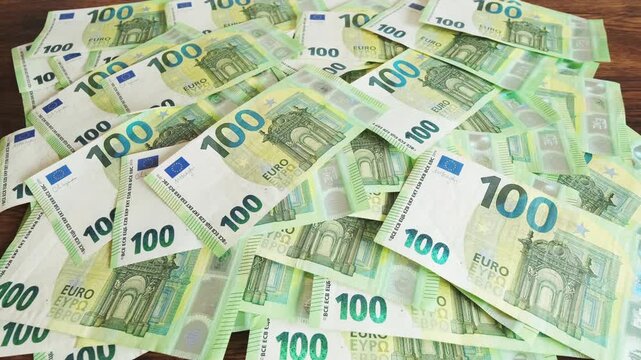 Pile of one hundred euro banknotes on wooden table. Cash background representing wealth, success and financial profit, 4k