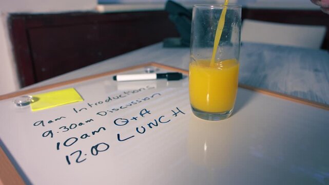 Pouring fresh orange juice at lunch break at meeting schedule on whiteboard