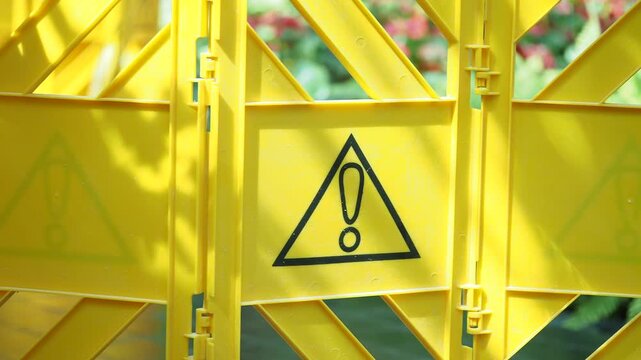 Yellow caution barrier with black triangle warning sign in public outdoor garden area motion footage