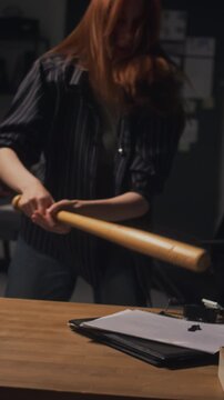 Vertical shot of young adult Caucasian woman working late on laptop, getting frustrated and smashing digital clock with baseball bat. Ideal for campaigns about employee burnout and workplace stress
