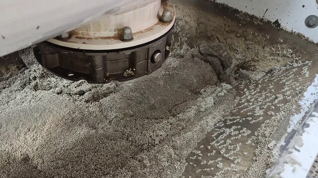Slow motion shot of a mechanical screw auger mixing lightweight polystyrene concrete inside a machinery hopper.