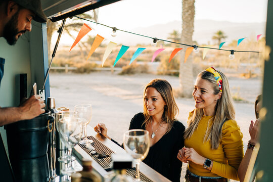 Man preparing cocktail for female clients in food truck