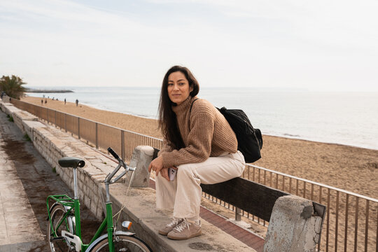 A woman is sitting near the beach with a bicycle next to her