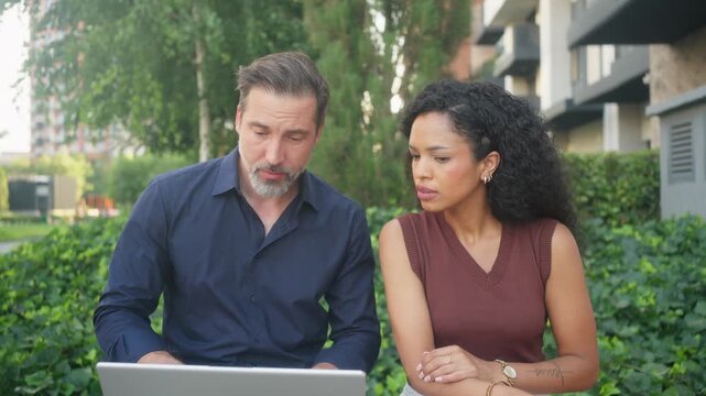 Business partners having discussion and different views while working on laptop outdoors