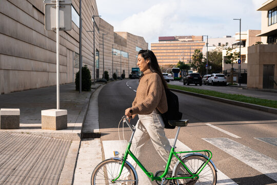 A woman walking across a crosswalk with a bicycle