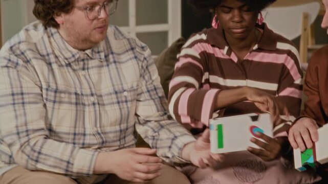 Diverse young adults sitting on sofa, examining retro VHS tapes and blowing dust off cassette. Video is perfect for nostalgia-themed marketing campaigns or retro technology promotions