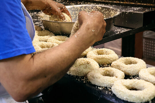 A baking artisan rolling unbaked bagels with sesame seeds