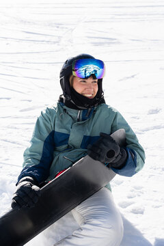 Happy woman holding snowboard sitting on snow mountain