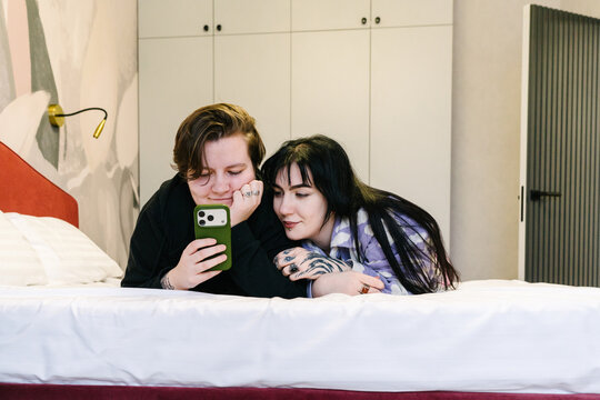 Two friends are looking at the phone, lying on the bed.